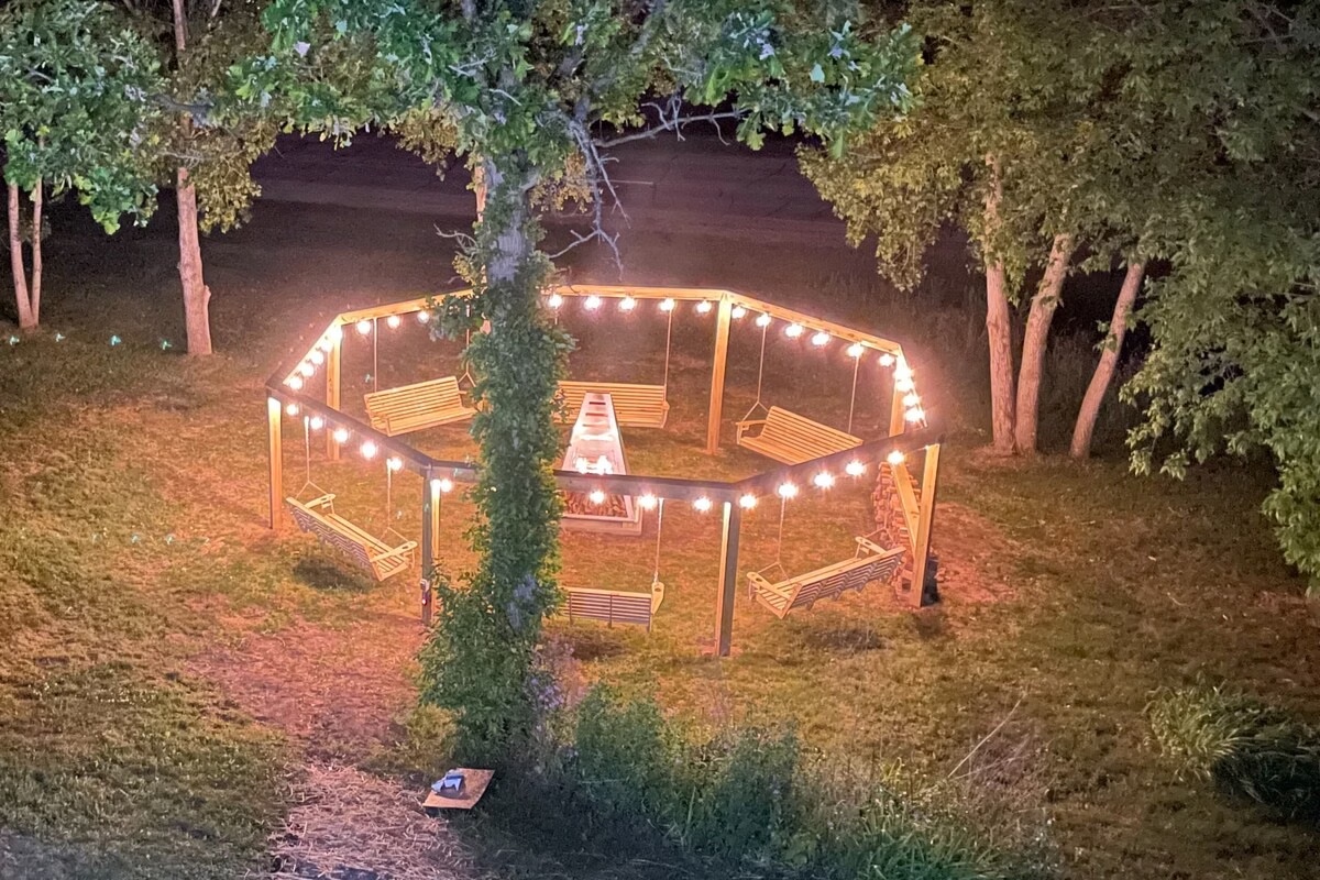 The octagon firepit at night — swings, string lights and fire